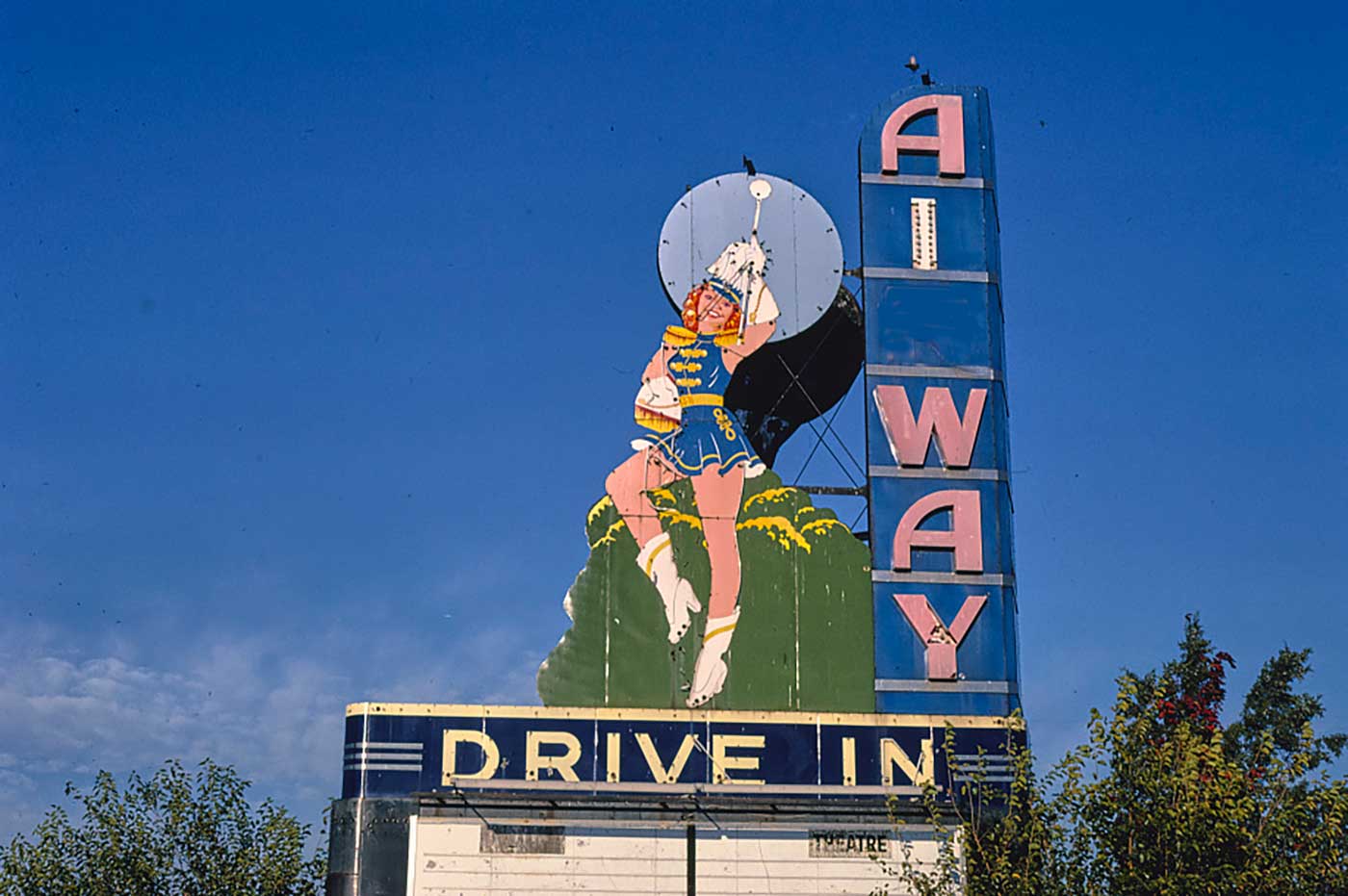 Old theater sign with a woman in a marching band uniform next to large letters reading vertically "AI WAY" below is an empty marquee for the movie title