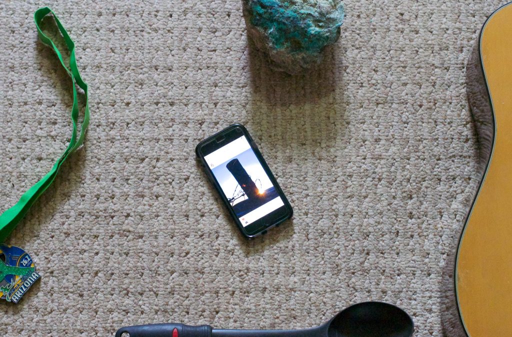 mobile phone with image of a fence post and a glint of light, on the edges are parts of objects such as a guitar, a rock, a half marathon medal, and a cooking sppon.